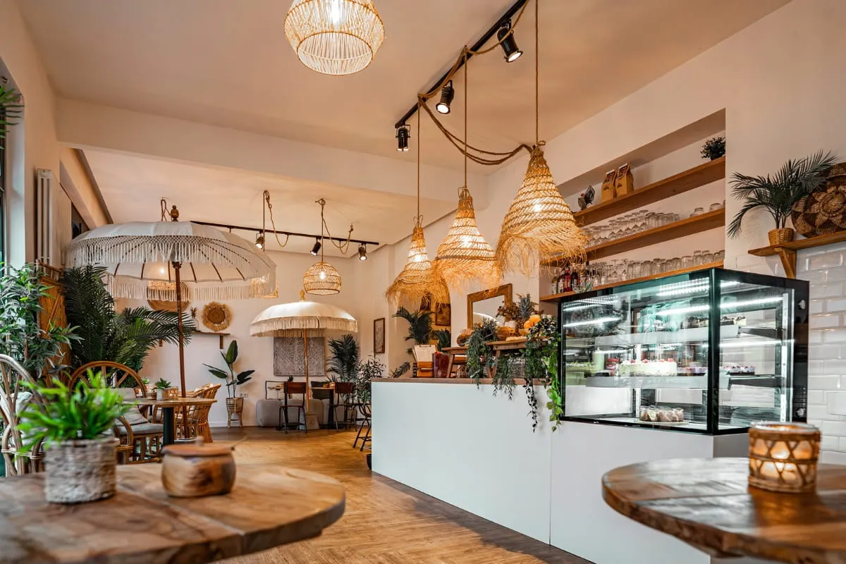 Theke mit Kuchenvitrine im Sorella Buer, davor Rattanstühle und ein Sonnenschirm