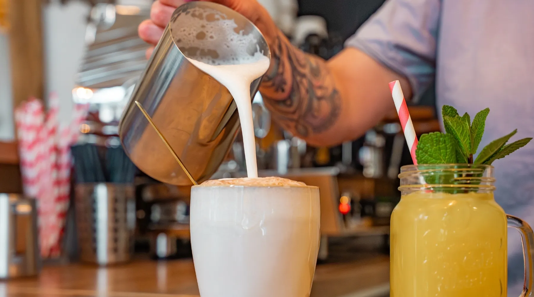 Milchschaum wird aus dem Kännchen in eine Tasse gegossen