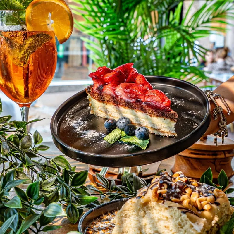 Cheesecake mit Erdbeeren neben einem Aperitif im Außenbereich