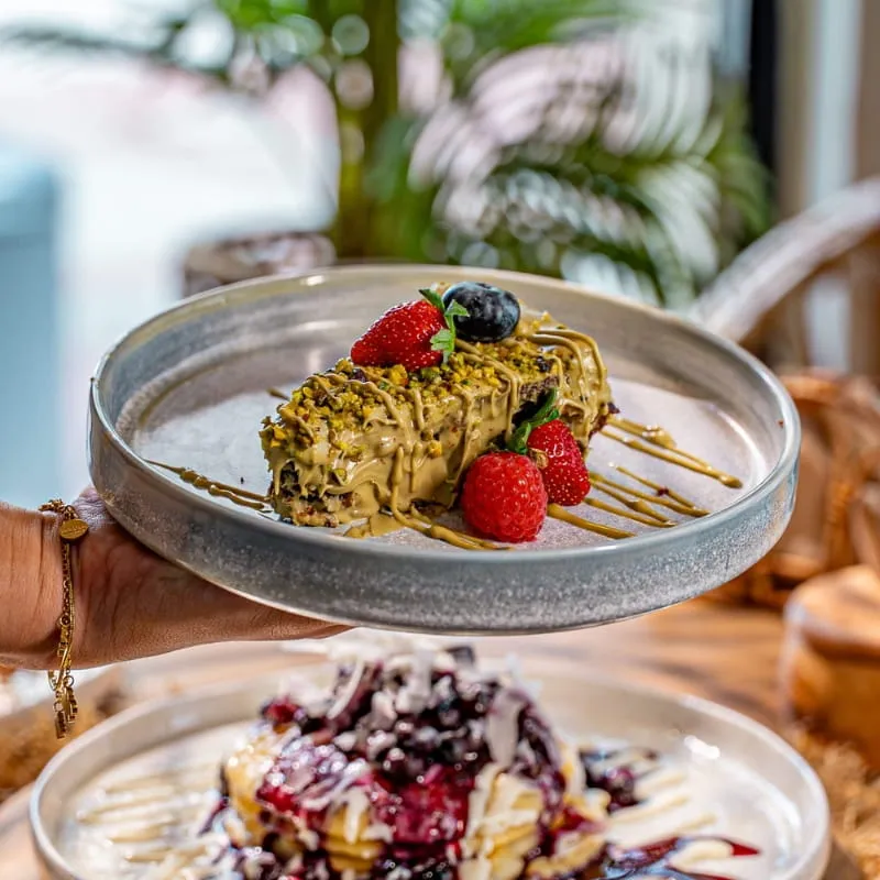 Zwei Teller mit Pistaziencreme und Beeren sowie Pancakes mit Heidelbeersoße