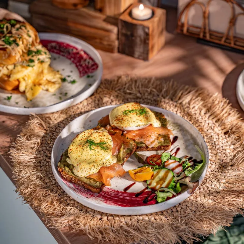 Eggs Benedict mit Räucherlachs, Radieschen und Salat, daneben ein Kaffee