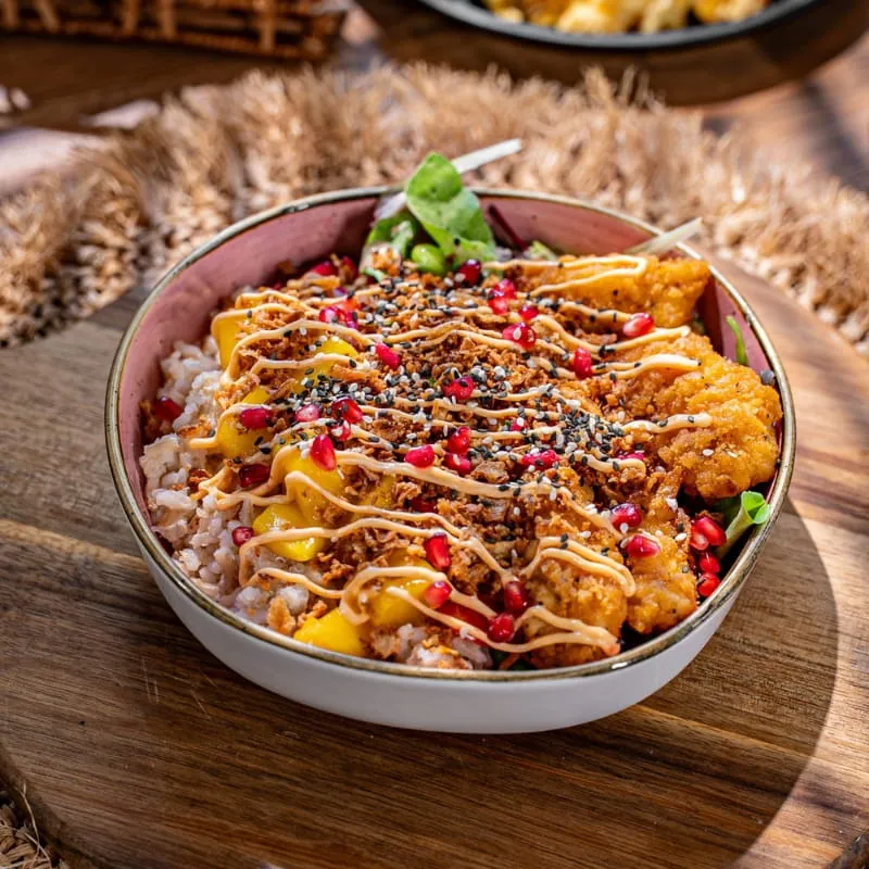 Bowl mit Mango, Granatapfel und Crunch auf einem Holzbrett
