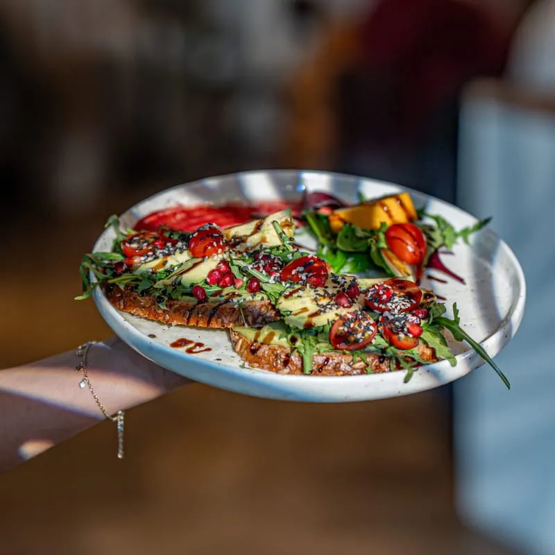 Avocadobrot mit Tomaten und Kräutern auf dunklem Holztisch