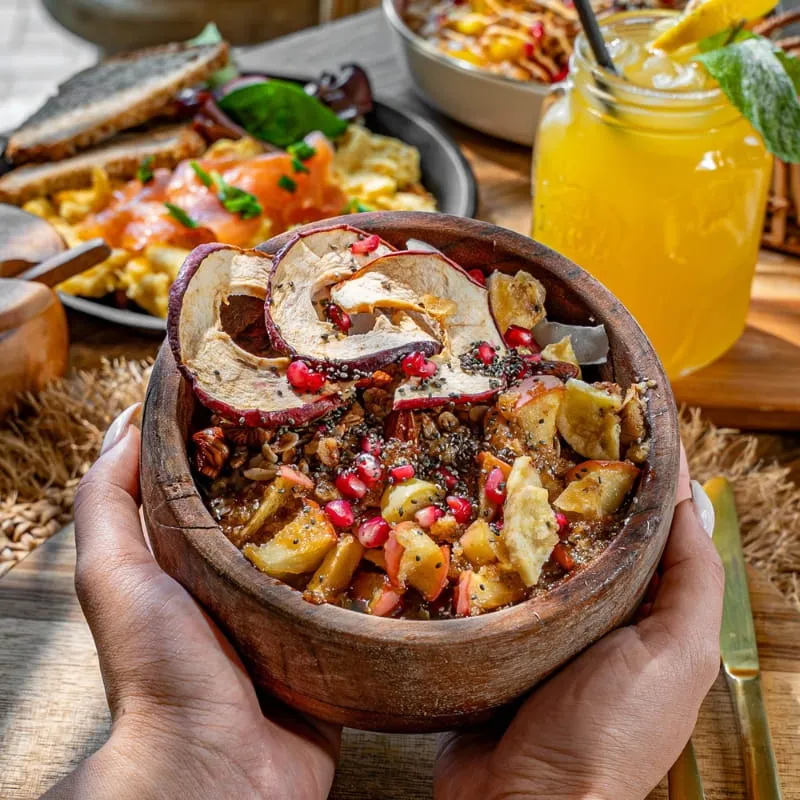 Hand hält eine Holzschale mit Apfelspalten, Granatapfelkernen und Granola
