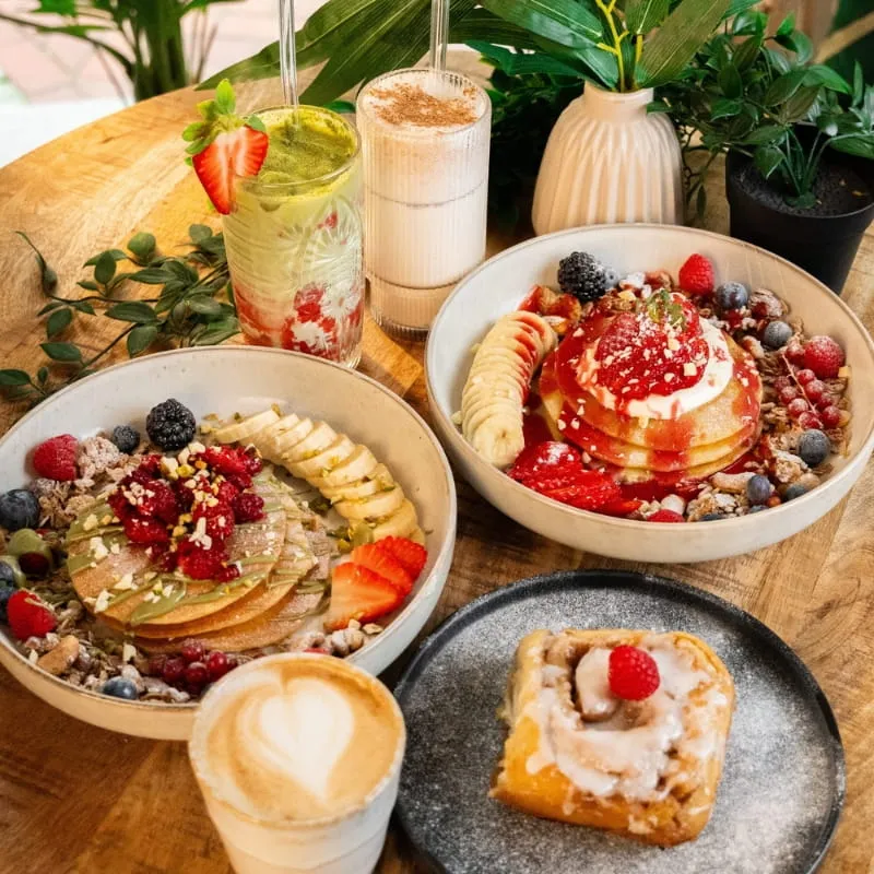 Gedeckter Tisch mit Bowls, Pancakes, Kuchen und Kaffee