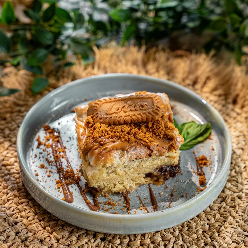 Zimtschnecke mit cremigem Frosting, Karamell, braunem Zucker und Lotus-Keks auf einem Teller
